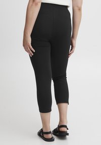 Leggings capri neri realizzati in materiale elastico, con una texture liscia e un alto punto vita. La lunghezza arriva a metà polpaccio.