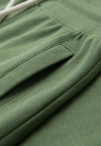 Groene katoenen joggingsbroek met een zijzak, elastische tailleband en een zachte textuur voor comfort. Naadtoespraken zichtbaar langs de randen.