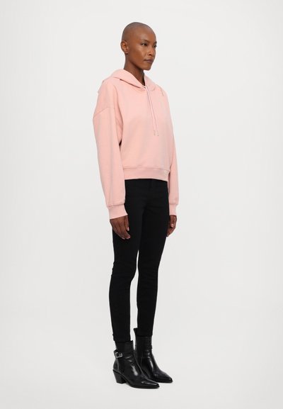 Hoodie cropped rosa com cordões, combinado com jeans skinny pretos e botins de salto pretos. Tecido suave com um ajuste descontraído.