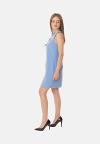 Vestito senza maniche di un azzurro chiaro con scollo alto e dettaglio a fiocco. Realizzato in tessuto liscio, abbinato a tacchi alti a punta neri.