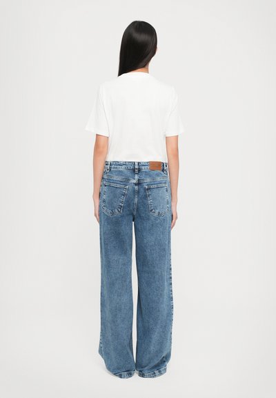 High-waisted wide-leg jeans in medium blue denim with a brown leather patch, featuring standard back pockets and a relaxed fit.
