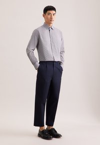 Licht geruit overhemd met knopen en een standaardkraag, gecombineerd met marineblauwe geplooide broek. Zwarte nette schoenen maken de outfit compleet.