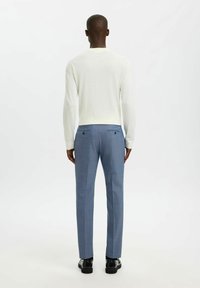 Chemise à manches longues de couleur claire associée à un pantalon bleu clair taillé, présentant une finition texturée et des poches arrière à deux boutons.