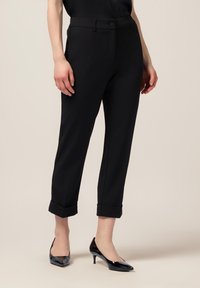 Svarta skräddarsydda byxor med slim fit, med uppvikt nederdel och knappstängning. Slät tyg med subtil textur, i kombination med spetsiga svarta klackar.