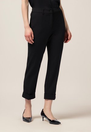 Pantalones negros de corte ajustado, con un dobladillo enrollado y cierre de botón. Tejido suave y textura sutil, combinados con tacones negros de punta.