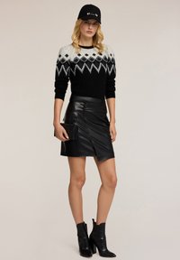 Maglione nero a maglia con un motivo a diamante bianco e grigio, abbinato a una gonna avvolgente in pelle nera. Accessoriato con una borsa a tracolla nera e stivali.