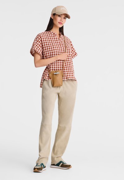 Red and white checkered short-sleeve shirt, beige trousers, brown and green sneakers, and a small tan crossbody bag. Beige cap worn.