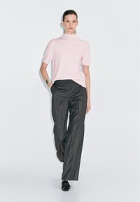 Pullover a manica corta rosa chiaro con colletto a imbuto abbinato a pantaloni larghi grigi scuri. Il modello indossa scarpe nere semplici e un bracciale d'argento. Design minimalista.