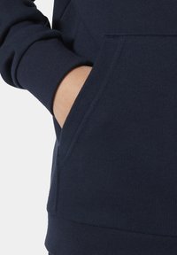 Sudadera de color navy con una tela texturizada, que cuenta con un bolsillo tipo canguro y puños acanalados. El diseño incluye una costura sutil a lo largo del hombro.