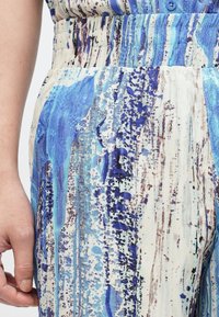 Modro-kremna tkanina z abstraktnimi črtami in lisami v različnih odtenkih. Podrobnost elastičnega pasu. Približen posnetek hlačnega dela.