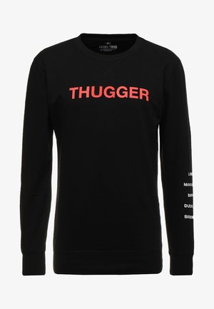 Czarna bluza z długim rękawem z czerwonym napisem „THUGGER” na piersi oraz białymi nazwami miast drukowanymi pionowo na prawym rękawie.
