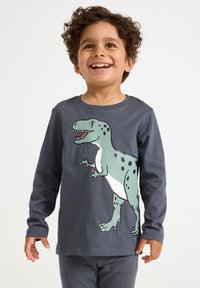 Smiling young boy with curly hair wearing a dark grey long-sleeve shirt featuring a large green cartoon dinosaur.