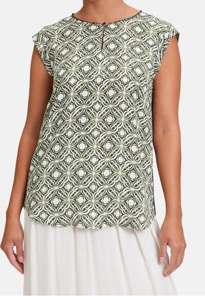 Femme portant un haut sans manches à motif géométrique vert et blanc avec une petite ouverture en forme de trou de serrure à l'avant et une jupe blanche.