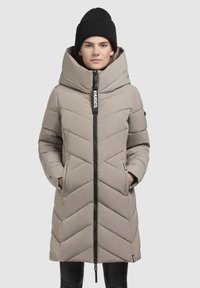 Padded coat in light beige with chevron pattern, large hood, and a black zipper. Features side pockets and a branded tag on the zipper pull.