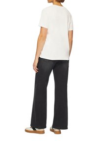 Witte t-shirt met korte mouwen, gecombineerd met hoge zwarte wijde jeans en witte schoenen met tan zolen. Eenvoudige, casual outfit.