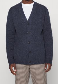 Námořnický kardigan, pletená textura, zapínání na knoflíky vpředu, design s V výstřihem, žebrované manžety a lem, kombinovaný s kostičkovanými kalhotami.