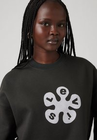 Dark green sweatshirt made of cotton, featuring a large, white graphic logo. The neckline is ribbed, and the fabric has a smooth texture.