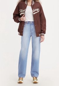 Brown satin varsity jacket with white lettering, paired with light blue wide-leg jeans and colorful sneakers.