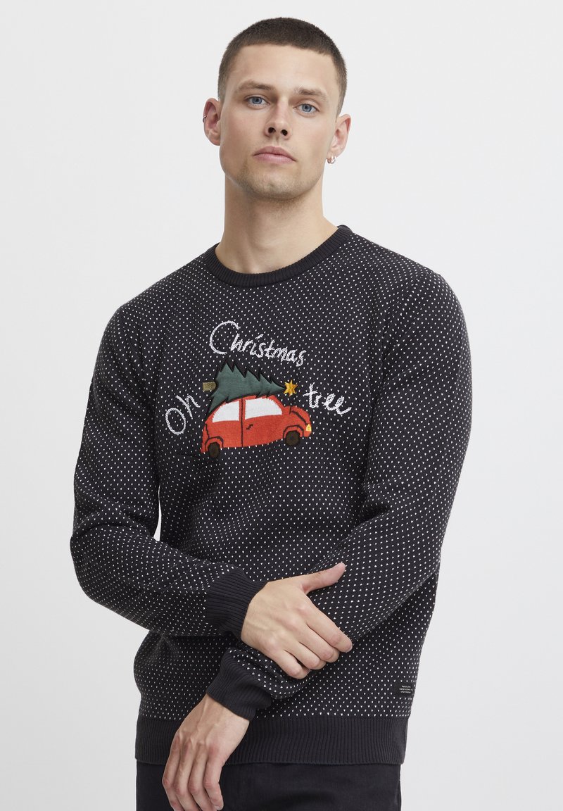 Maglione lavorato a maglia nero con pois bianchi, auto rossa ricamata con albero di Natale e testo "Oh albero di Natale" in un design informale.