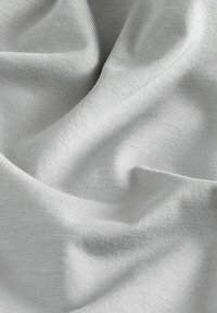 Tissu gris clair avec une texture lisse, présentant de douces draperies et un subtil nervurage. Le matériau semble extensible et léger.