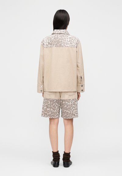 Μπεζ μπουφάν με λεοπάρ σχέδιο στο πάνω μέρος, συνδυασμένο με μπεζ σορτς με λεοπάρ εκτύπωση. Διαθέτει γιακά και μανσέτες με κουμπιά.