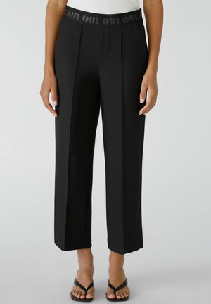 Schwarze maßgeschneiderte Hosen mit weitem Bein, versehen mit einem strukturierten Bund mit "OUI"-Muster. Glattes Gewebe mit einer eleganten Oberfläche.