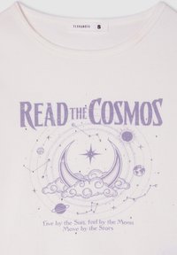 Biała koszulka z krótkim rękawem z bawełny z fioletowym nadrukiem tekstu "CZYTAJ KOSMOS" w towarzystwie wzorów niebieskich, w tym księżyców, gwiazd i planet.