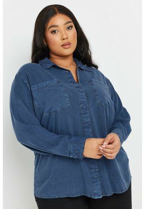Denim shirt in dark blue, featuring a button-down front, two chest pockets, long sleeves, and a relaxed fit with a curved hem.