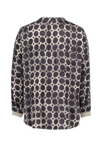 Long-sleeved blouse in a light fabric featuring a cream base with large black polka dots. Round neckline with subtle cuff detailing.