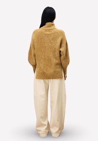 Oversized beige wollen trui met een hoge kraag, voorzien van losse mouwen, gecombineerd met hoog gesloten, wijde crème broek.