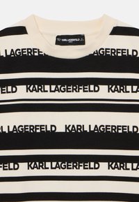 Melna un krēmkrāsas svītrainā T-kreklā ir atkārtota "KARL LAGERFELD" zīmola nosaukuma izlase. Gluda tekstūra ar ribotu apaļu kaklu un īsām piedurknēm.