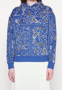 Felpa con cappuccio blu caratterizzata da motivi paisley in bianco e nero, dotata di tasca a marsupio e polsini e orlo ribattuti.