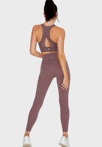 Top sportivo aderente e leggings in un tenue color mauve. Il reggiseno presenta un design a schiena scoperta e un dettaglio con taglio. Texture liscia con vita alta.