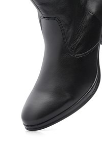 Bottine en cuir noir avec bout arrondi, coutures visibles et finition lisse sur fond blanc.