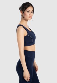 Marineblauwe sportbh met brede banden en een gladde textuur, voorzien van een subtiele contrasterende naad langs de buste en bijpassende high-waisted legging.
