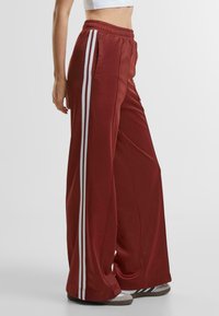 Wide-leg pants in burgundy satin with white side stripes, featuring an elastic waistband and side pockets for comfort and ease of movement.