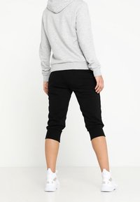 Sweat à capuche gris associé à un pantalon jogging noir court. Baskets blanches avec des accents ajourés. Tous les articles ont une coupe décontractée et une texture douce.