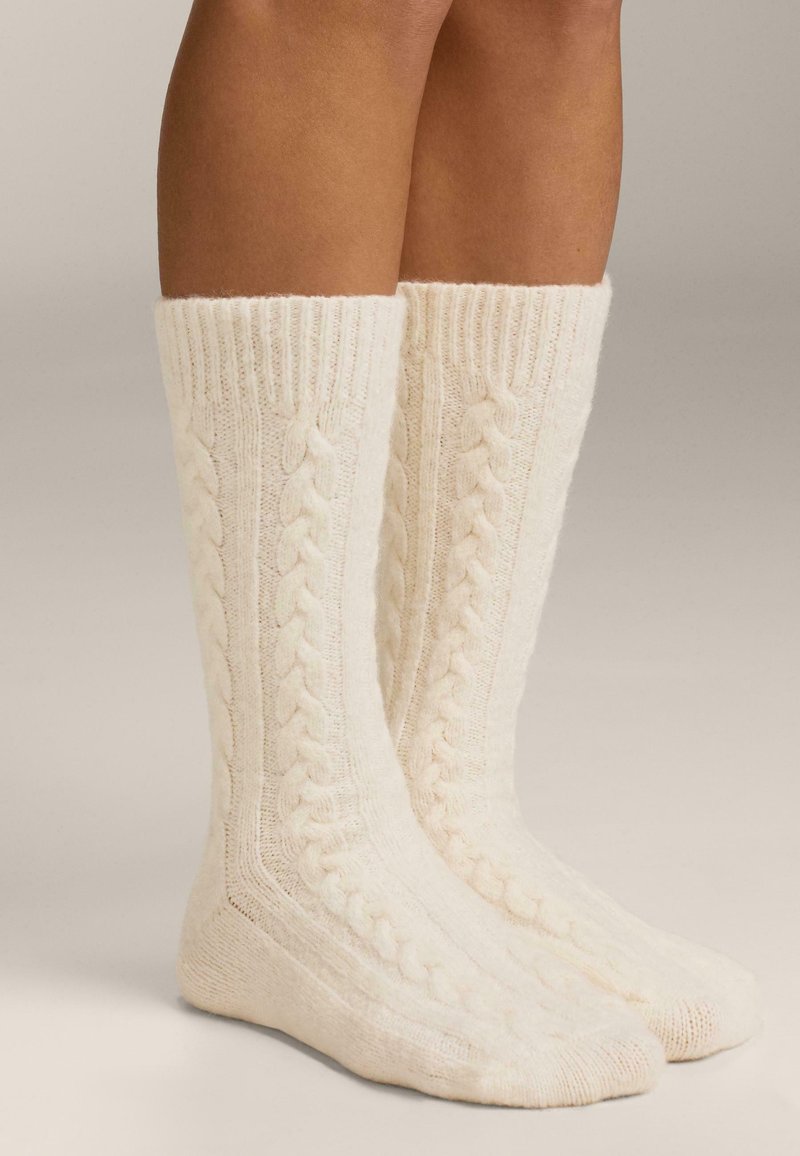 Nogavice do kolen v krem barvi z vzorcem pletenja v obliki kablov in rebrastimi manšetami, izdelane iz mehke, teksturirane tkanine.