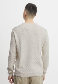 Beige knitted sweater featuring a textured pattern and ribbed cuffs, with a classic crew neck design and long sleeves.