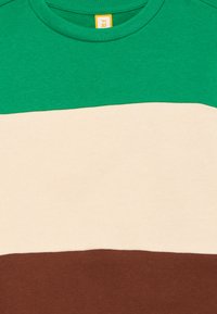 Groene, beige en bruine horizontaal gekleurde blokken crewneck shirt stof close-up met zichtbare halslijn en label.