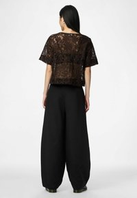 Kort bruin kanten topje met korte mouwen en een bloemenpatroon, gecombineerd met losse zwarte palazzo-broeken. De outfit heeft een ontspannen silhouet en een zachte textuur.