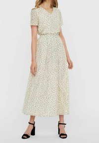 Robe longue crème à col en V et manches courtes, ornée d'un motif de petits pois noirs éparpillés, cintrée à la taille pour une coupe fluide.