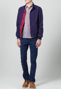 Tmavě modré chino kalhoty, béžové brogue boty, kostkovaná košile v bílé a modré barvě a fialová bunda s červenou podšívkou a knoflíky.