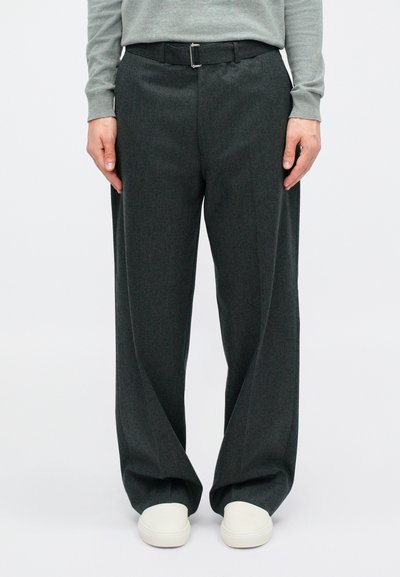 Tumed hallid laiad püksid, millel on ristküliku kujuline nööp ja sile tekstuur. Sobitatud valgete slip-on kingadega.