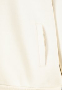 Hellbeige Sweatshirt aus strukturiertem Material. Verfügt über eine seitliche Tasche mit einer Nahtdetail und einem gerippten Bund. Weiches, lässiges Design.