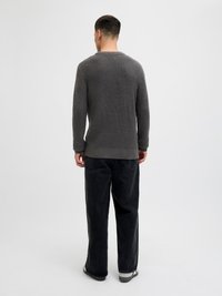 Gray knitted sweater with a textured pattern, paired with loose-fitting black jeans and dark footwear, viewed from the back.