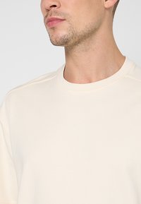 Lichtbeige sweatshirt met korte mouwen, een ronde halslijn, een gladde textuur en zichtbare stiksel details bij de naden.