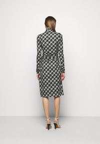 Sukienka w czarno-białą kratę, z długimi rękawami, wysokim kołnierzem, dopasowanym w pasie, sięgająca do kolan, zestawiona z białymi sandałami na wysokim obcasie z paskami.