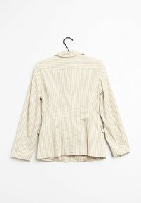 Beige randig skjorta med långa ärmar, knäppt krage och sid sömmar. Har vertikala ränder med lätt textur. Hänger på en svart krok.