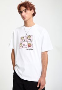 Hvid bomulds t-shirt med et farverigt grafik, der viser tegneserie ansigt og tekst, rund halsudskæring og korte ærmer. Brandlogo i bunden.